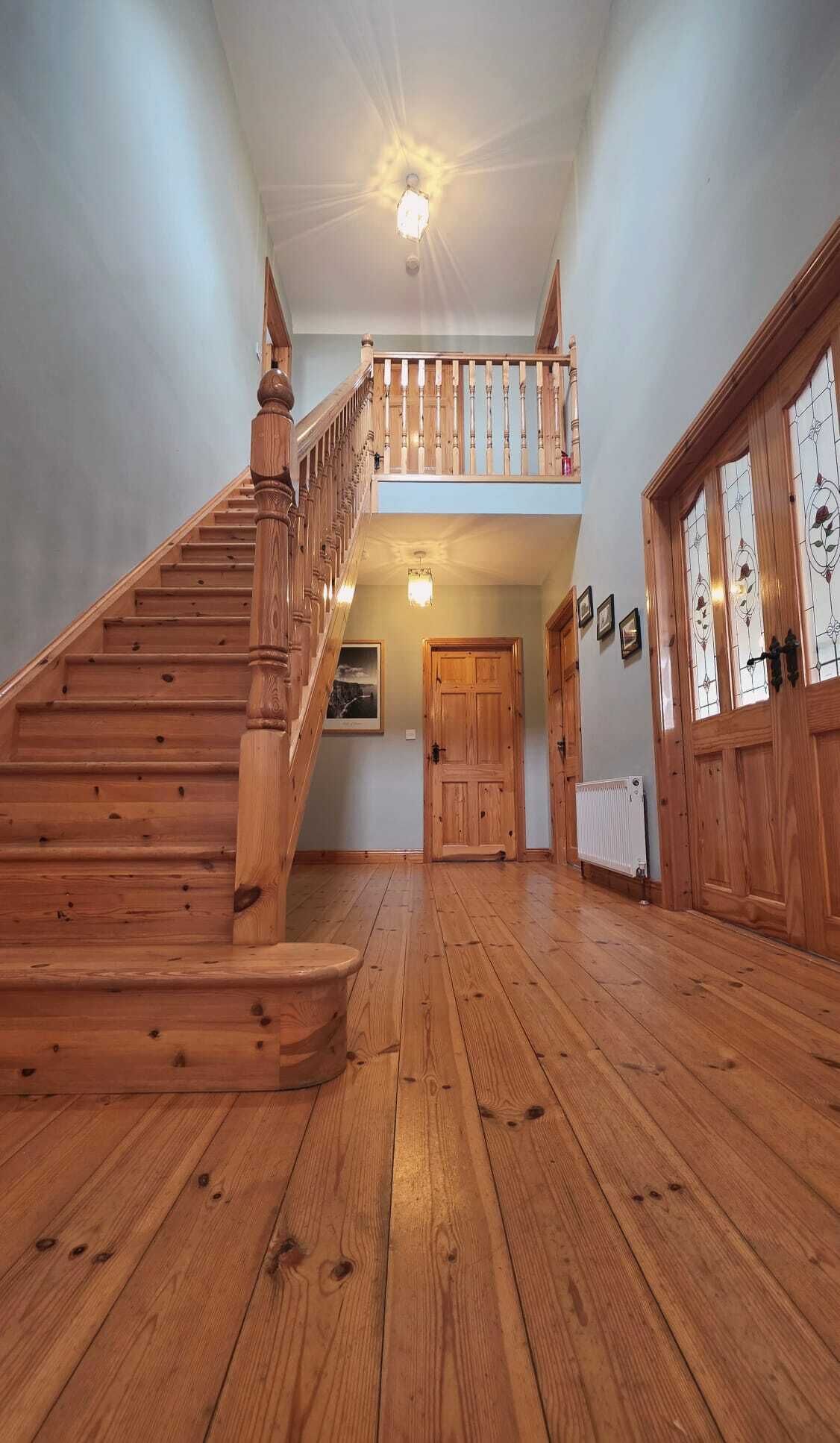 A wooden staircase leading to an upper level with a balcony, a wooden door, and a radiator on the floor.