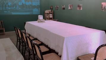 Un salón de conferencias con una larga mesa, sillas, una pantalla de proyector y un ventanal.