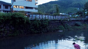 Vista al río con un edificio moderno, un puente de madera y una persona de pie sobre una plataforma de concreto.