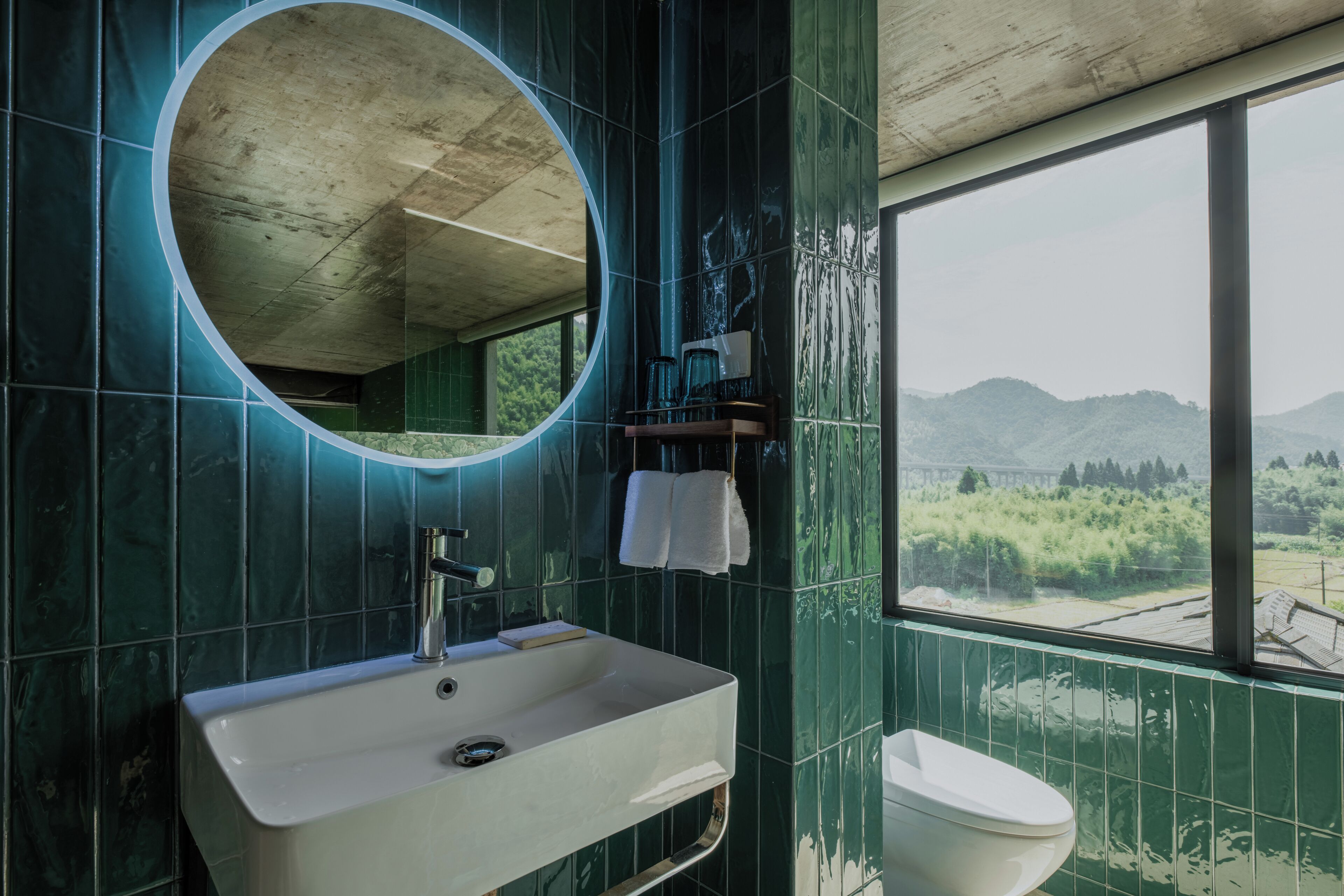 Een badkamer met een grote spiegel, een wastafel en een toilet. Een raam biedt uitzicht op een bergachtig landschap.