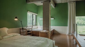 Una habitación con cama, escritorio, silla y ventana, con vistas a zonas verdes.