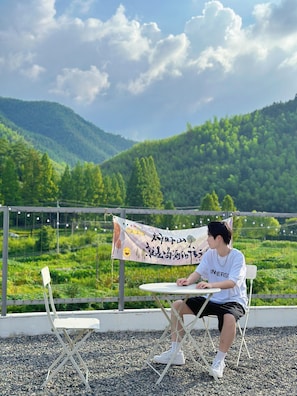 A person seated at a table with a banner in the background, overlooking a mountainous landscape. - Mogan Mountain Dibeli-in the fields (Huzhou)