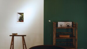Una habitación con un caballete de madera, un cuadro enmarcado en la pared, una pared verde y un estante con objetos decorativos.