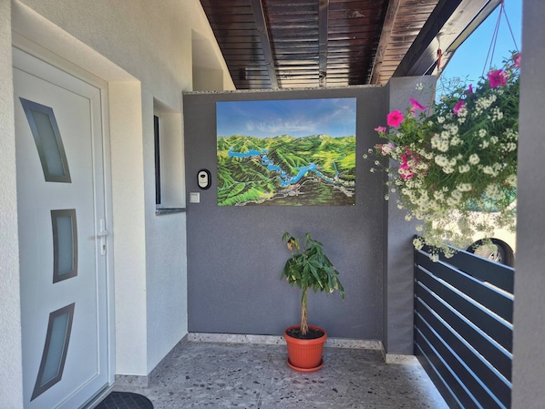 A modern exterior with a potted plant, a framed landscape painting, and a metal gate.