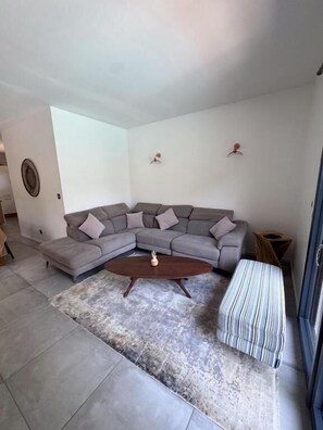 A living room with a grey sectional sofa, a round coffee table, and a striped ottoman.
