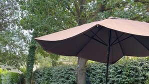 Une terrasse extérieure avec une table et des chaises, un banc et un grand parasol.