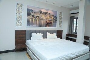 A hotel room with a bed, a large framed picture of a palace, and a window with curtains. - The Moti Plaza (Udaipur)