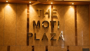 Paredes com a inscrição 'THE MOTI PLAZA' em letras metálicas, um ventilador de teto e iluminação embutida.