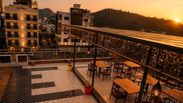 Terraço no telhado com área de estar externa e vista para a cidade ao pôr do sol.