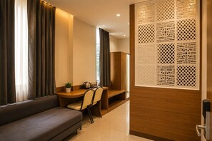 Una habitación de hotel moderna con un sofá, un escritorio de madera y un biombo decorativo.