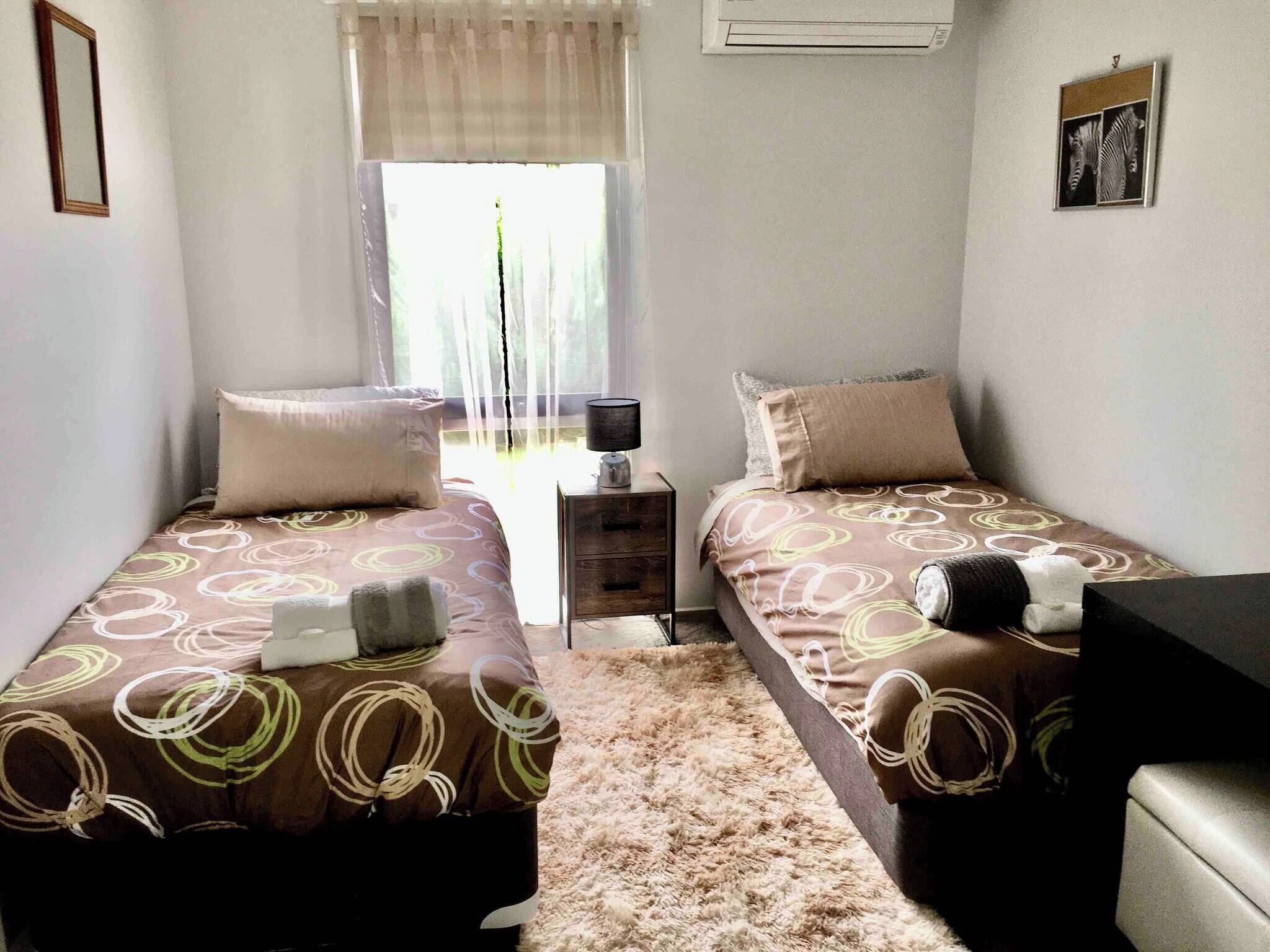 A twin bedroom with two beds, a nightstand, a lamp, and a window with curtains.