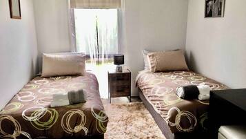 A twin bedroom with two beds, a nightstand, a lamp, and a window with curtains.