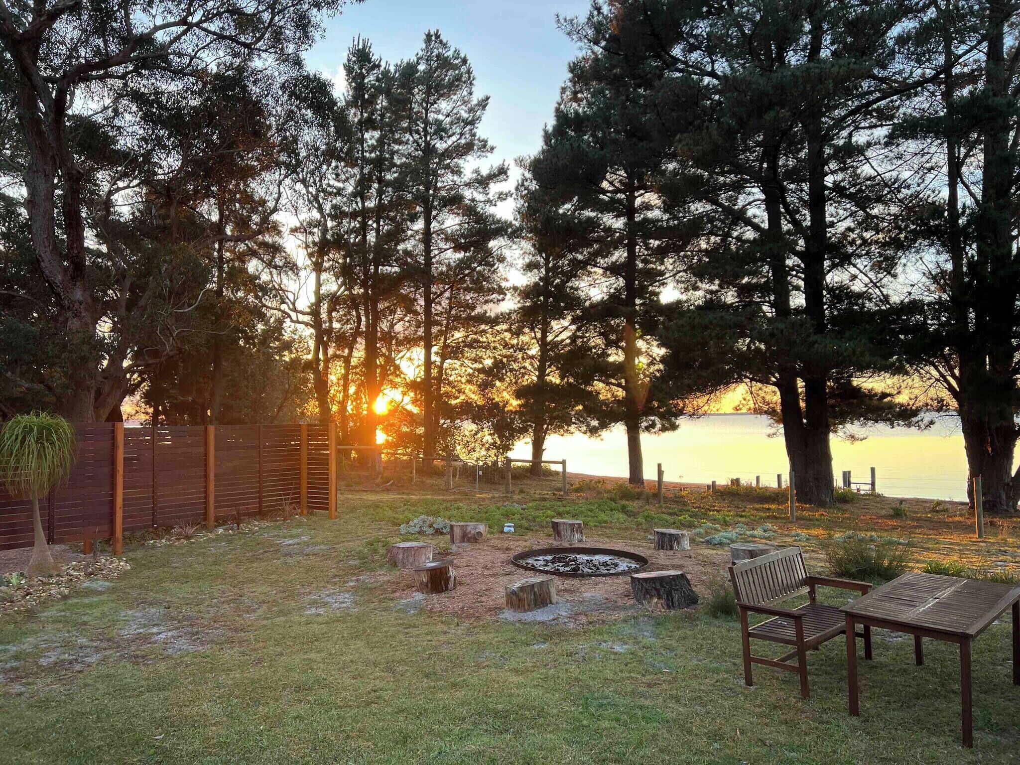 A serene outdoor setting with a fire pit, seating, and a view of the sunset over a body of water.