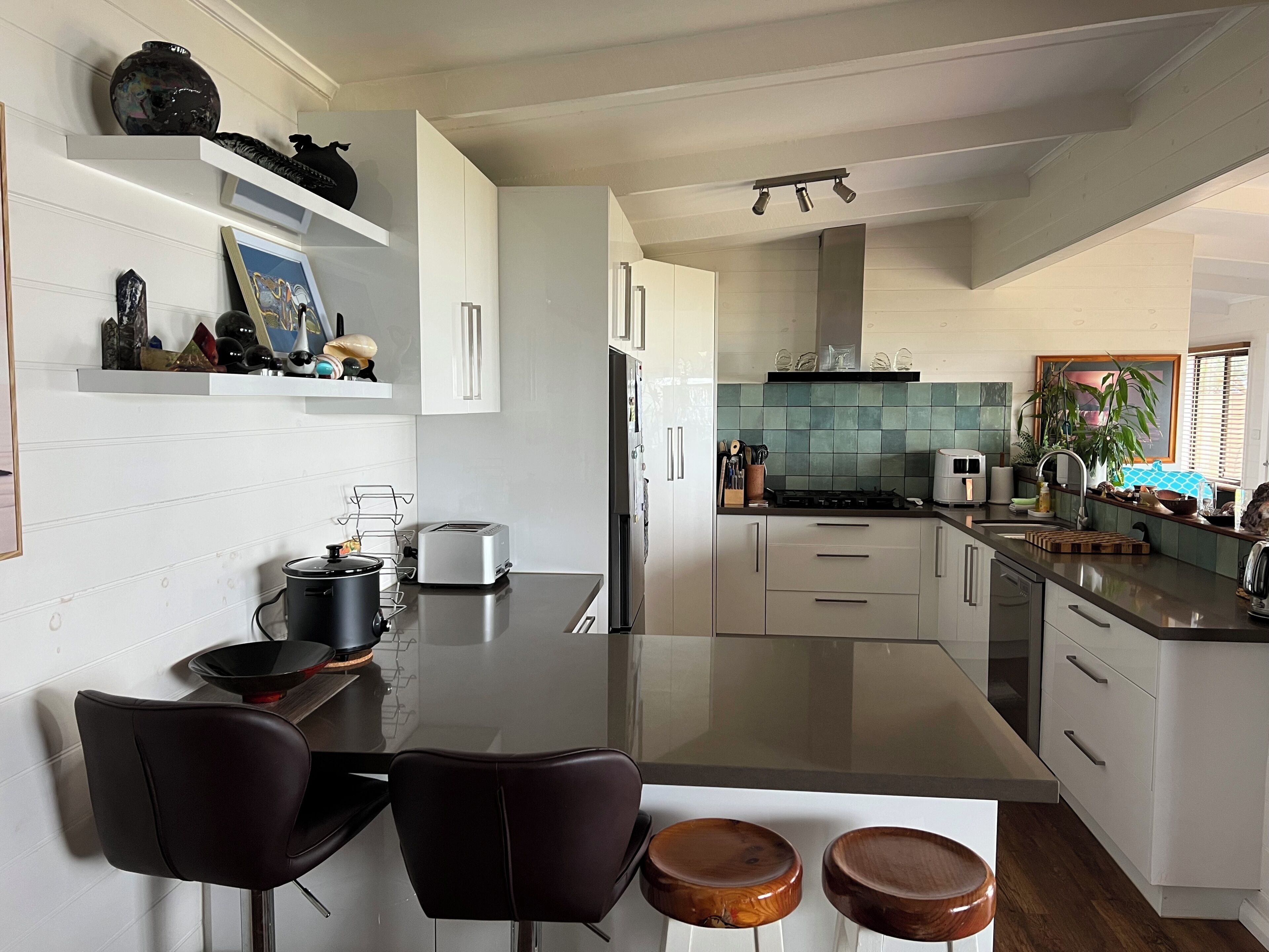 A modern kitchen with white cabinetry, a black countertop, and a dining area with a glass table and two chairs.