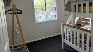 A room with a crib, a window with blinds, a fan, and a wall-mounted TV.