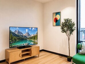 A modern living room with a flat-screen TV on a wooden TV stand, a potted plant, and a colorful abstract painting on the wall. - Southbank 2BR 2Bath | Free Parking & Balcony (Southbank)