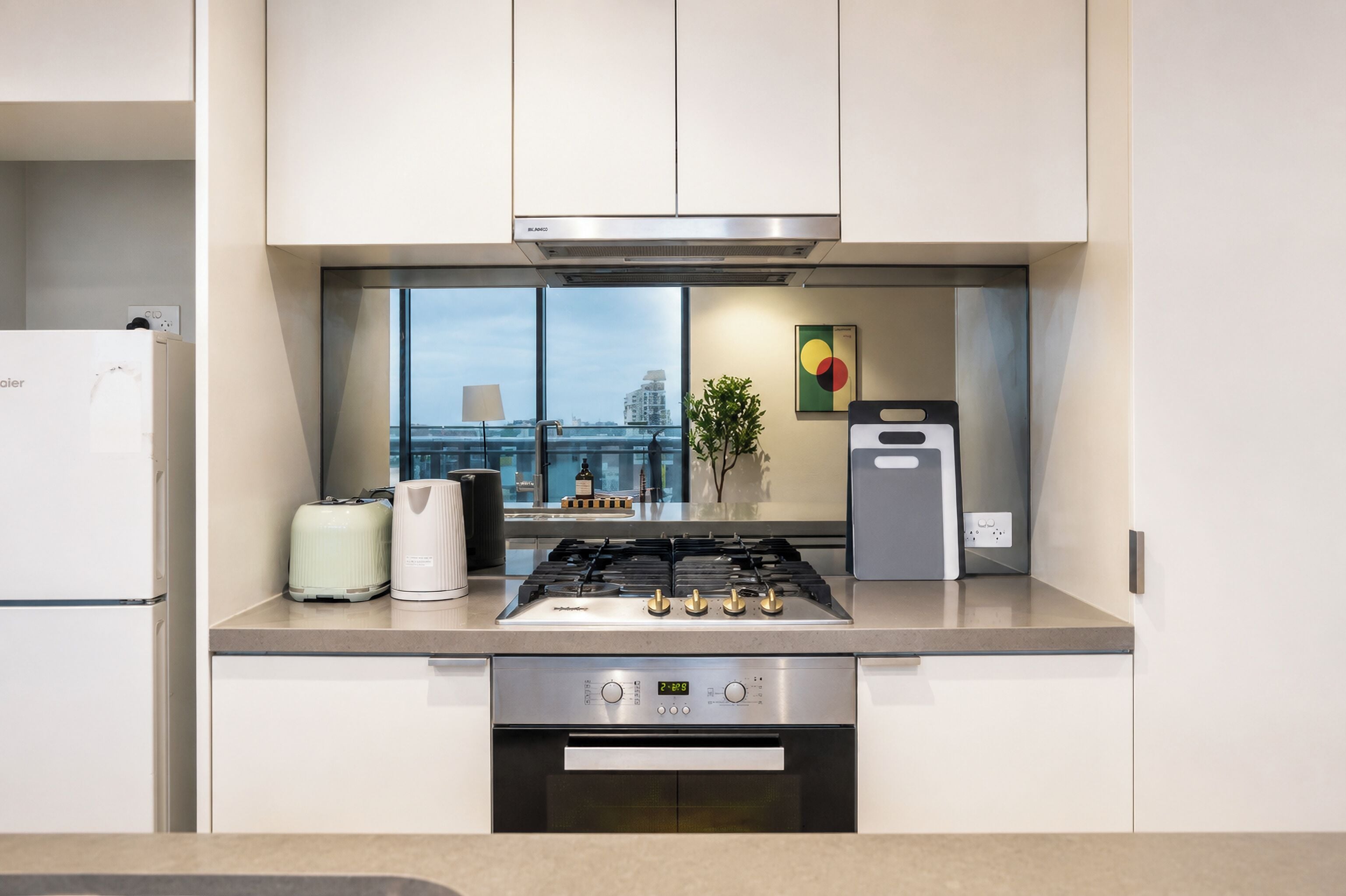 A modern kitchen with a gas stove, oven, and a view of the city through large windows.
