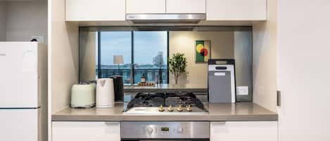 A modern kitchen with a gas stove, oven, and a view of the city through large windows.