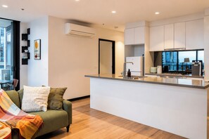A modern apartment with a kitchenette, a sofa with a blanket, and a view of the city through large windows. - Southbank 2BR 2Bath | Free Parking & Balcony (Southbank)