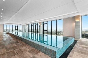 A modern indoor swimming pool with a clear view of the cityscape through large windows. - Southbank 2BR 2Bath | Free Parking & Balcony (Southbank)