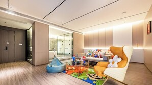 Un hall d’hôtel moderne doté d’un espace détente comprenant un tapis à motifs de Mario, un fauteuil en forme de sac et une collection de figurines de Mario.