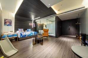Quarto de hotel moderno com uma cama grande, área de estar com mesa de vidro e banheiro separado com banheira.