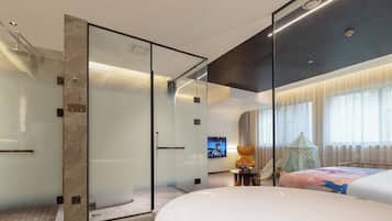Una habitación de hotel moderna con ducha de vidrio, una bañera grande y un televisor montado en la pared.
