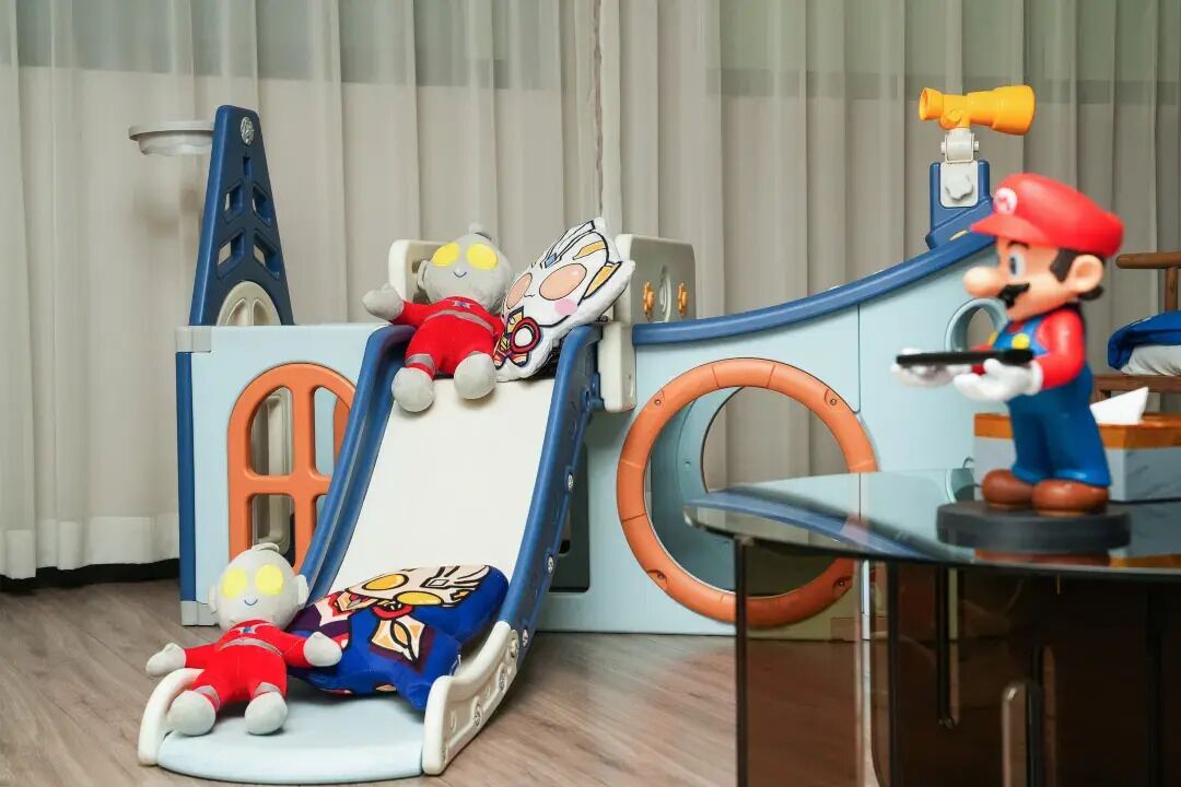 Zona de juegos infantiles con un tobogán, una figura de juguete que se parece a Mario, y un juguete que recuerda a un personaje de Tom y Jerry.