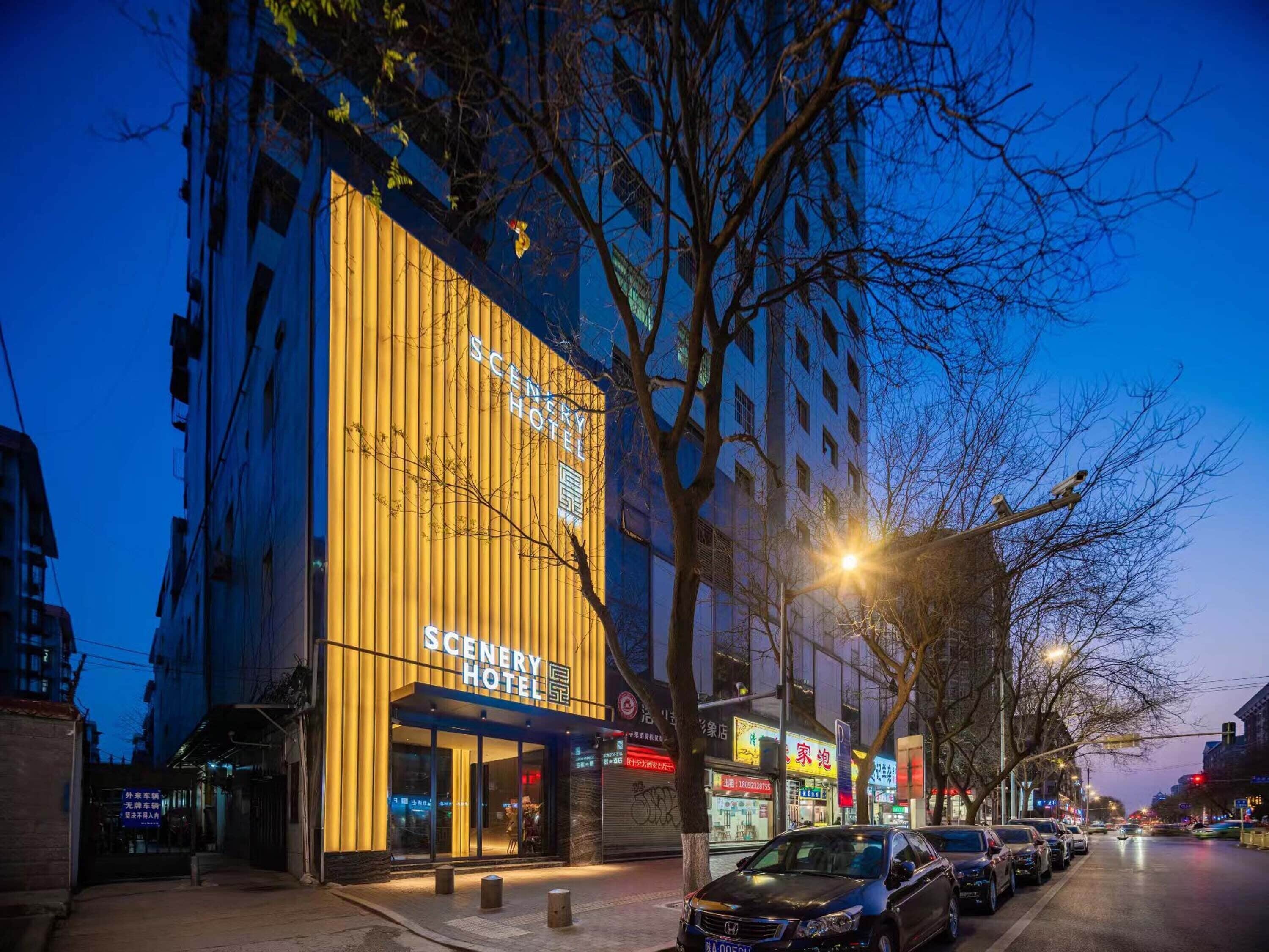 A hotel with a prominent yellow facade and signage, located on a city street with parked cars and trees.