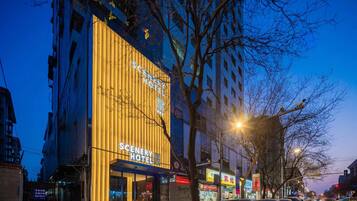 A hotel with a prominent yellow facade and signage, located on a city street with parked cars and trees.