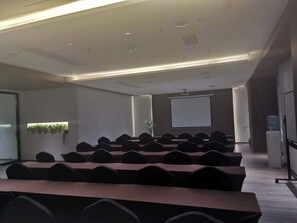 Uma sala de conferência com uma mesa comprida, várias cadeiras, uma tela de projetor e um bebedouro.