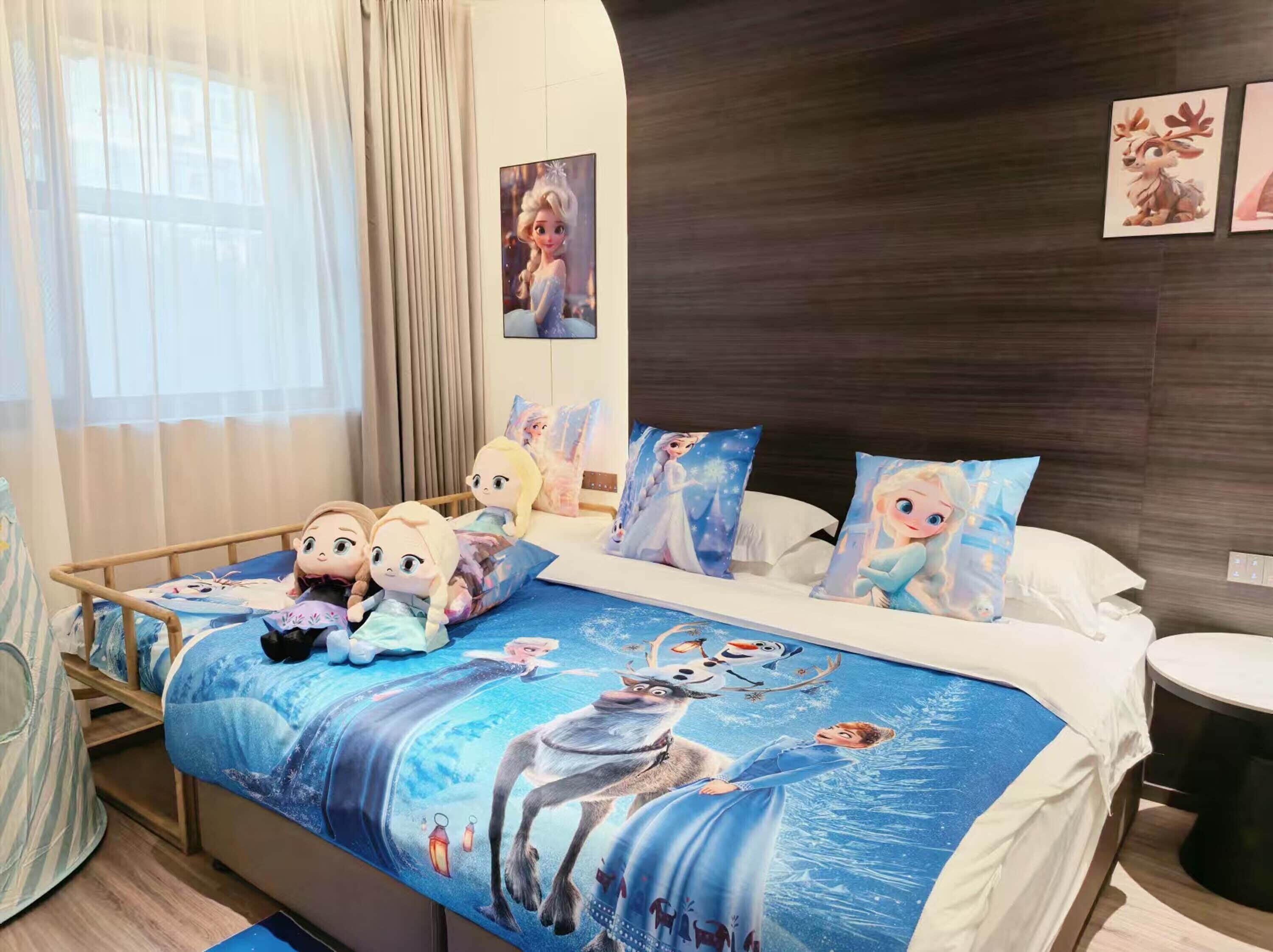 A hotel room with a bed featuring a Frozen-themed bedspread, pillows, and plush toys.