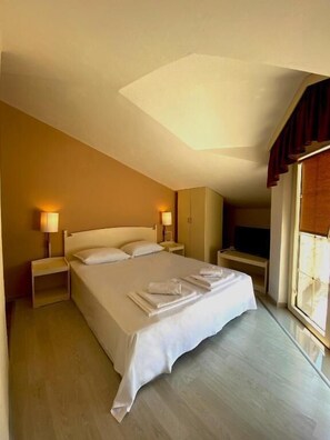 A hotel room with a large bed, bedside lamps, a TV, and a window with curtains. - H Kleopatra (Ulcinj)