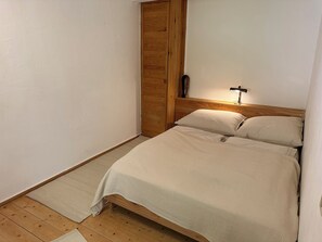 A bedroom with a bed, wooden wardrobe, and a bedside lamp.