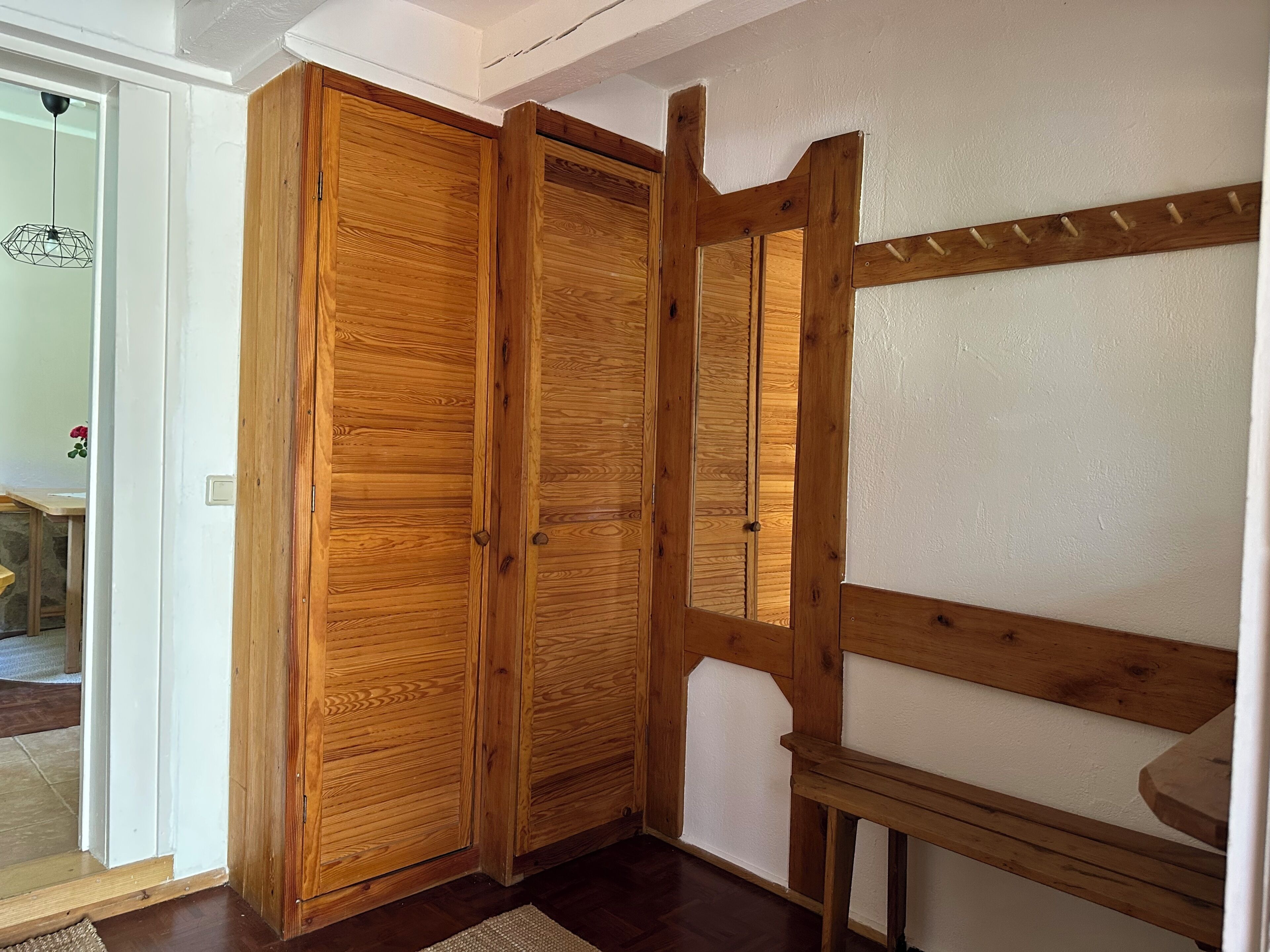 Une armoire en bois avec une porte miroir, un banc en bois et un mur blanc.
