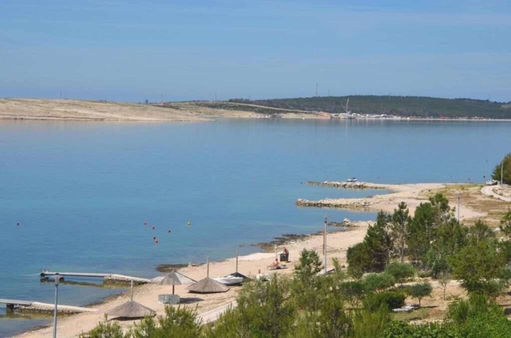 Uma área costeira com céu claro, uma praia de areia e algumas estruturas que parecem ser cabanas ou abrigos de praia.