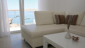 Ein modernes Wohnzimmer mit einer Couch und einem Couchtisch, Meerblick durch große Fenster und ein Balkon mit Geländer.