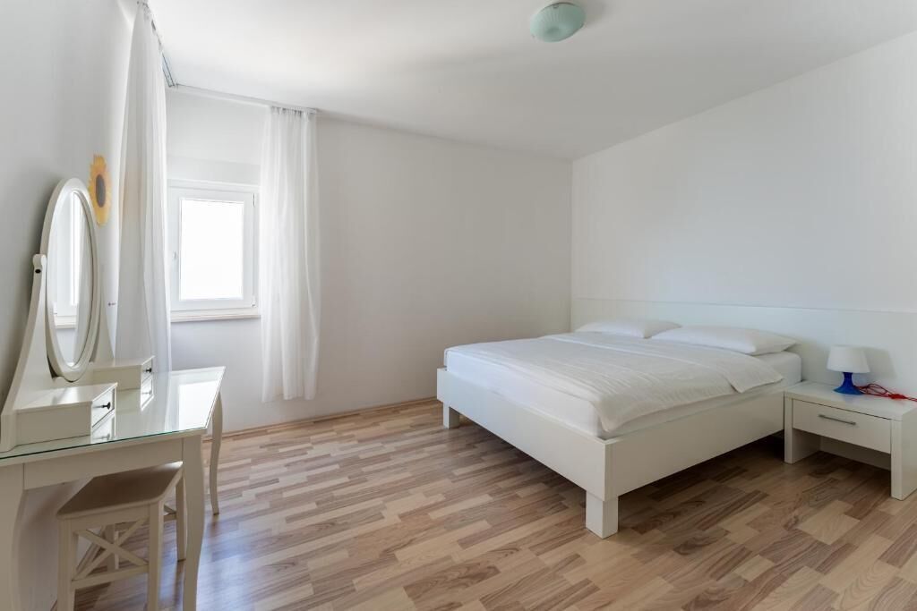 A bedroom with a bed, a bedside table with a lamp, a dresser with a mirror, and a window with curtains.