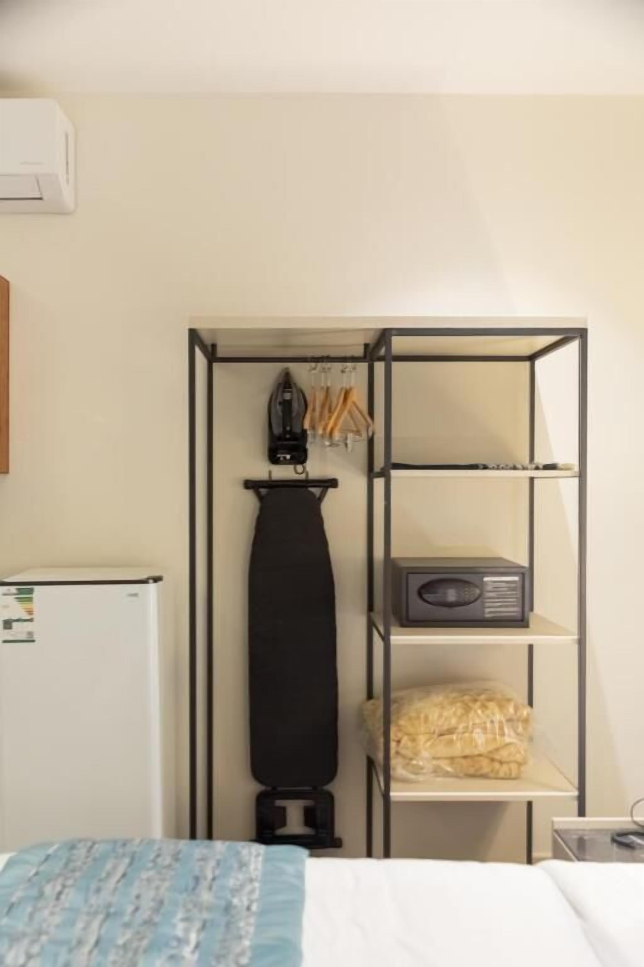 A compact room with a bed, a radiator, a shelf with a radio, and a hanging iron.