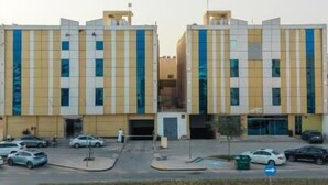Un edificio moderno con fachada simétrica, múltiples ventanas y un estacionamiento al frente.