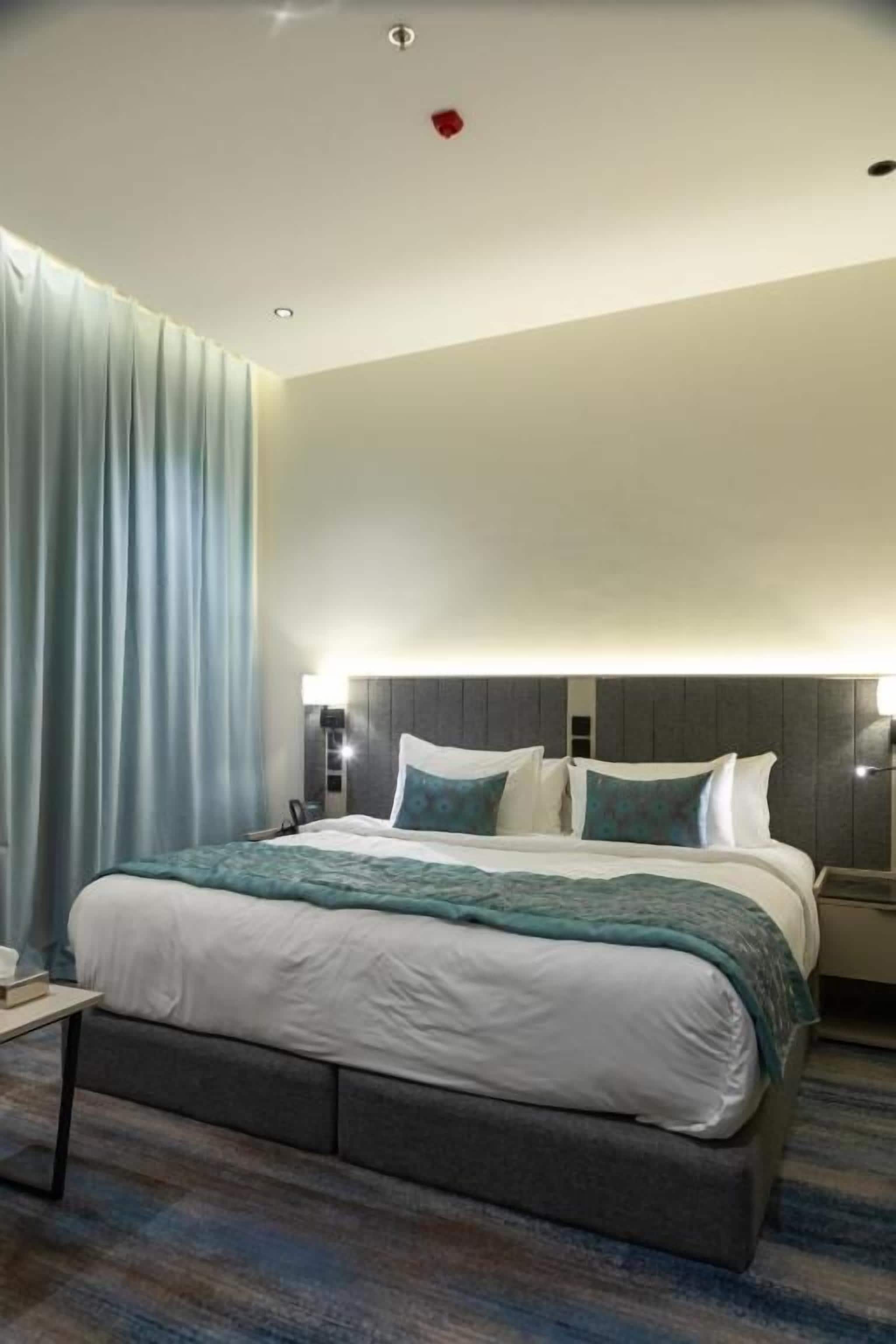 Une chambre d’hôtel avec un grand lit, une table de chevet, une petite table et une tête de lit dotée d’un éclairage intégré.