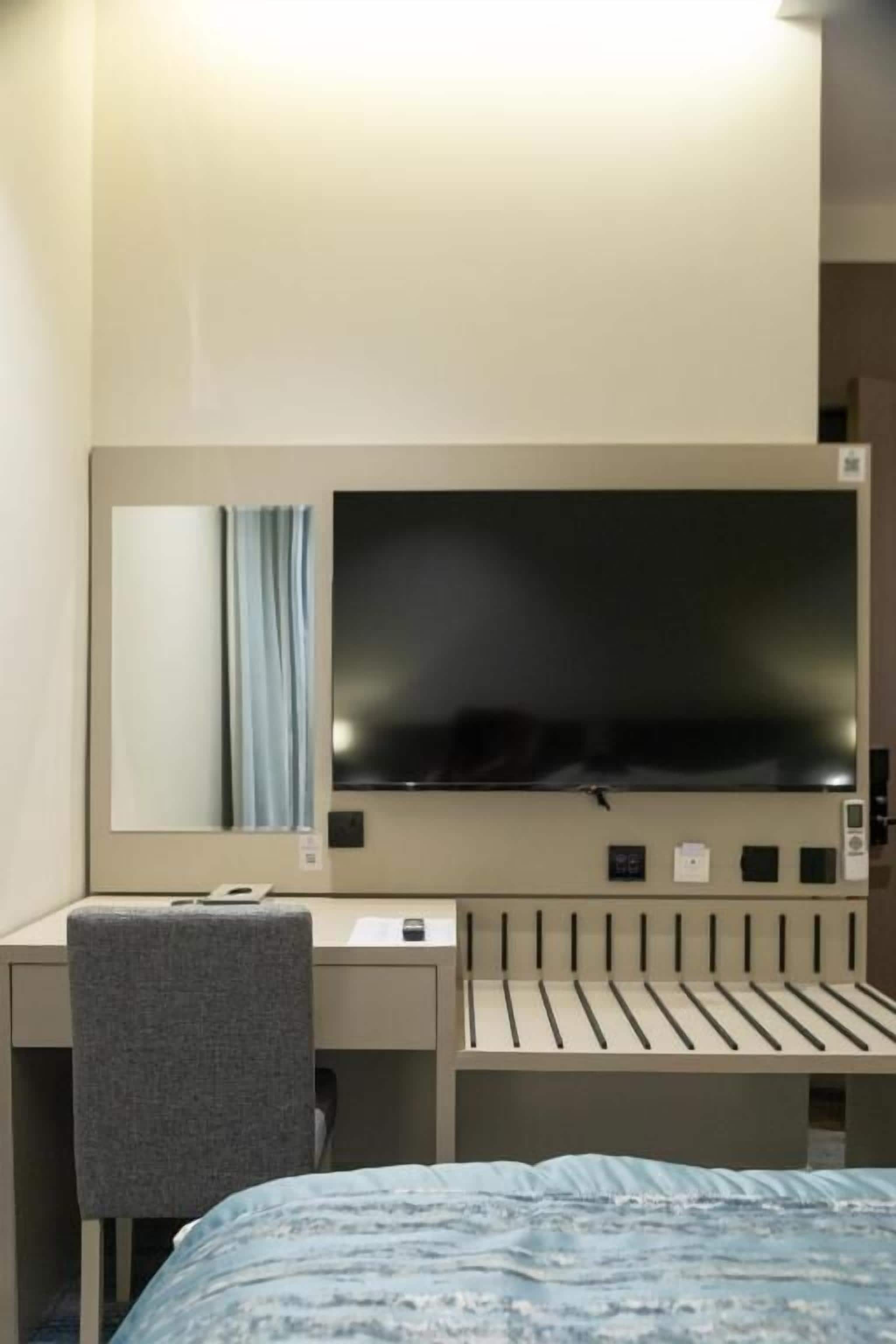 Ein Hotelzimmer mit Bett, Schreibtisch, Stuhl, Fernseher und einem Fenster mit Vorhängen.