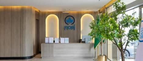 A hotel reception area with a reception desk, a plant, and a sign with the hotel's name.