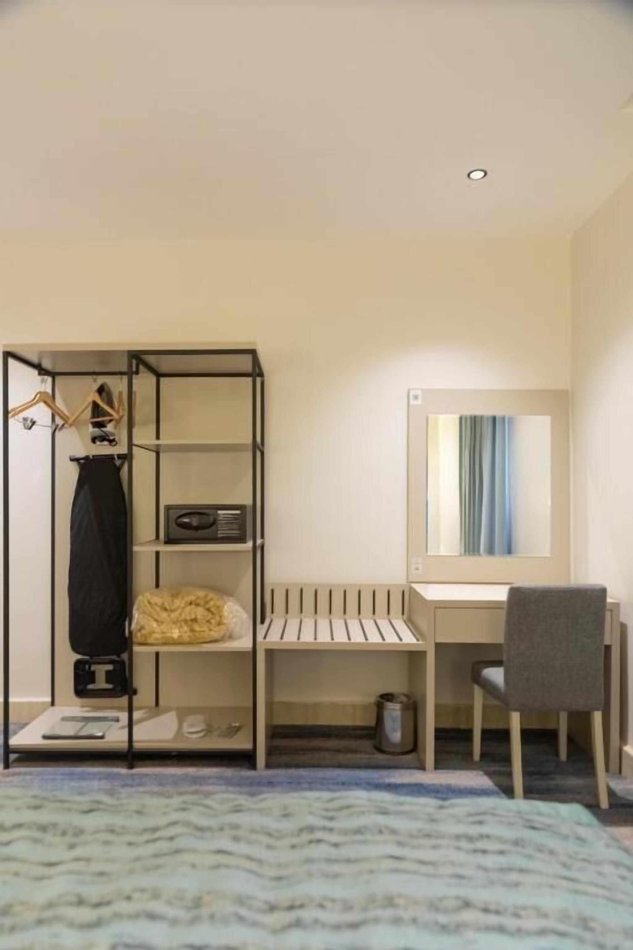 A hotel room with a bed, a desk with a chair, a wardrobe, and a mirror.