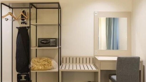 Una habitación de hotel con cama, escritorio, silla, armario y espejo.