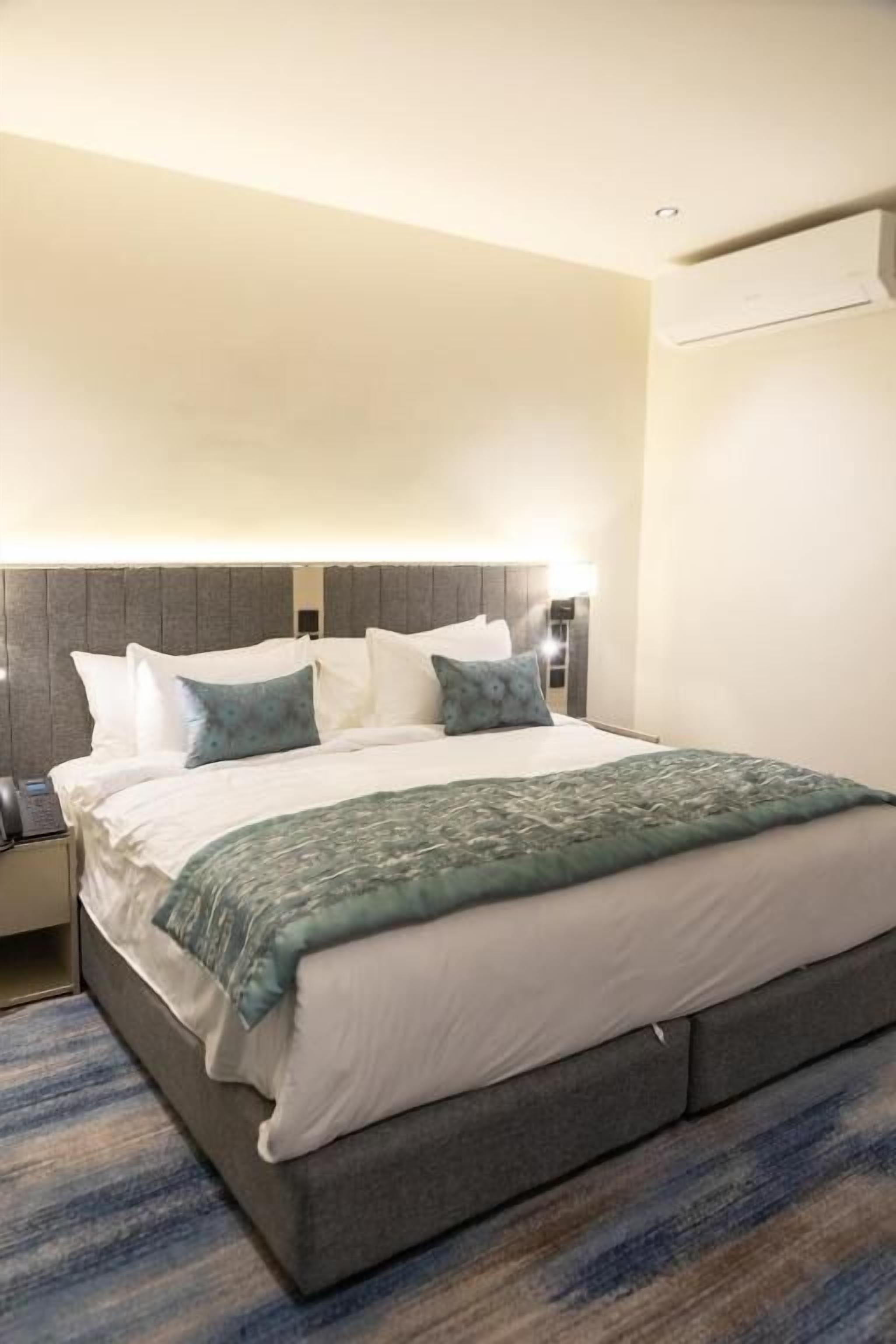 A hotel room with a large bed, a headboard, a bedside table, and a nightstand.
