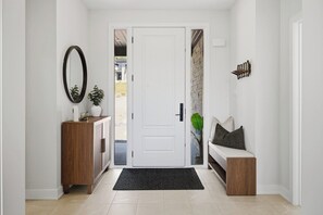 Ein Flur mit einer weißen Tür, einem Holzschrank, einer Bank und einem schwarzen Teppich.
