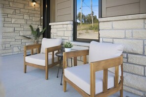 A patio with two wooden chairs and a small table, a potted plant, and a view through a window. - LOB Wellness Retreat-Hot Tub-Sauna-Games-Fire Pit (Lake of Bays)