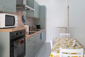 A compact kitchen with a microwave, oven, and sink. There's a dining table with a floral tablecloth and a chair. - Bright Apt with View near Vatican - Casa Alice (Roma)