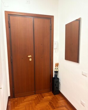 Une porte double en bois fermée, dotée d’un trou de serrure et d’un petit cadenas, une boîte de rangement noire contenant des parapluies et un téléphone fixé au mur.